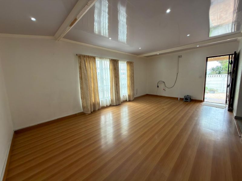 Spacious, empty living area featuring laminate flooring, recessed downlighting, and direct access to the exterior through a security gate.