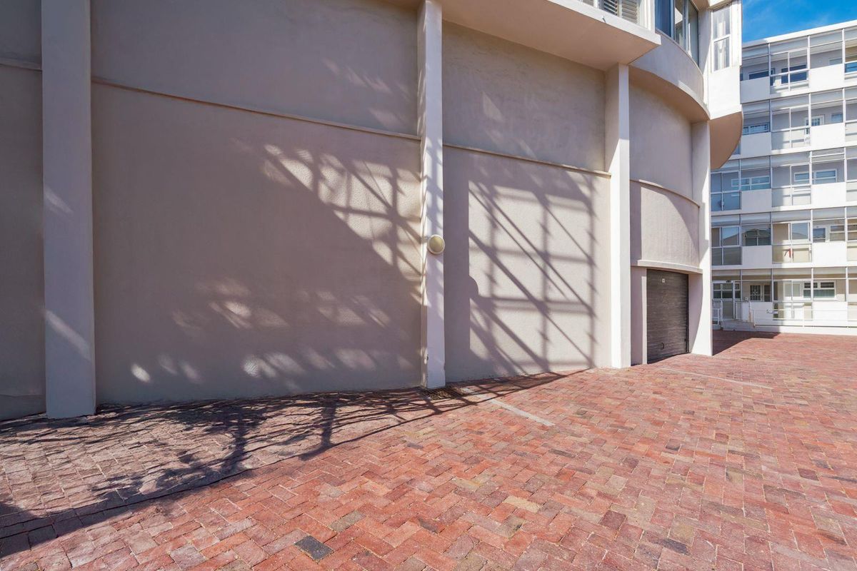 A view of the rear exterior area featuring brick paving, a garage entrance, and a curved building facade.