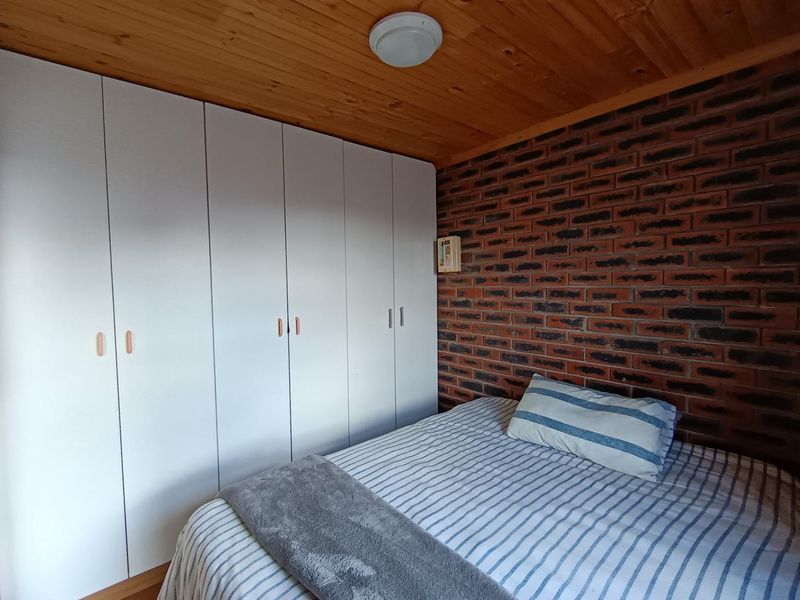 A bedroom featuring a distinctive exposed brick wall, timber ceiling, and extensive white built-in cupboards providing ample storage space.