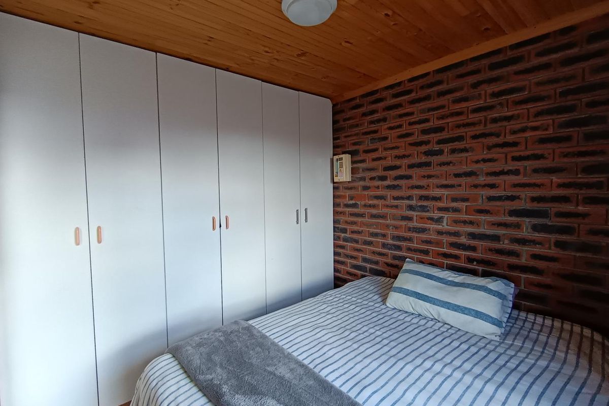 A bedroom featuring a distinctive exposed brick wall, timber ceiling, and extensive white built-in cupboards providing ample storage space.