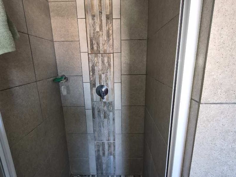 A clean, modern shower enclosure featuring neutral wall tiles with a decorative vertical accent strip and mosaic floor tiling.
