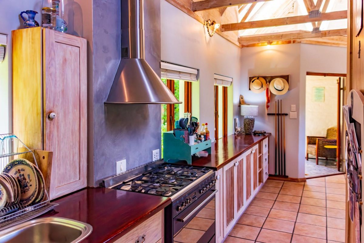 A rustic-style kitchen featuring exposed timber roof trusses, wooden countertops, a gas stove with a stainless steel extractor, and tiled flooring.
