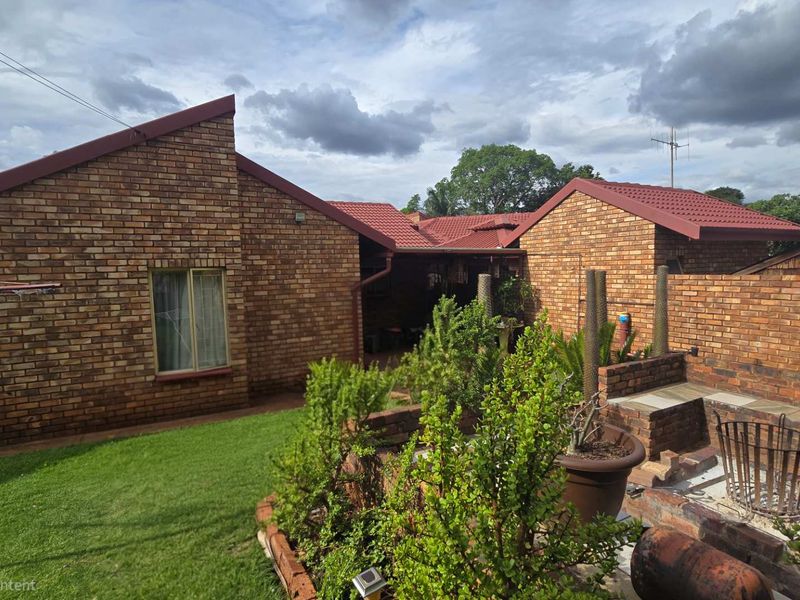 Rear view of the property featuring a face brick facade, tiled roof, and a built-in brick braai area set within a garden.