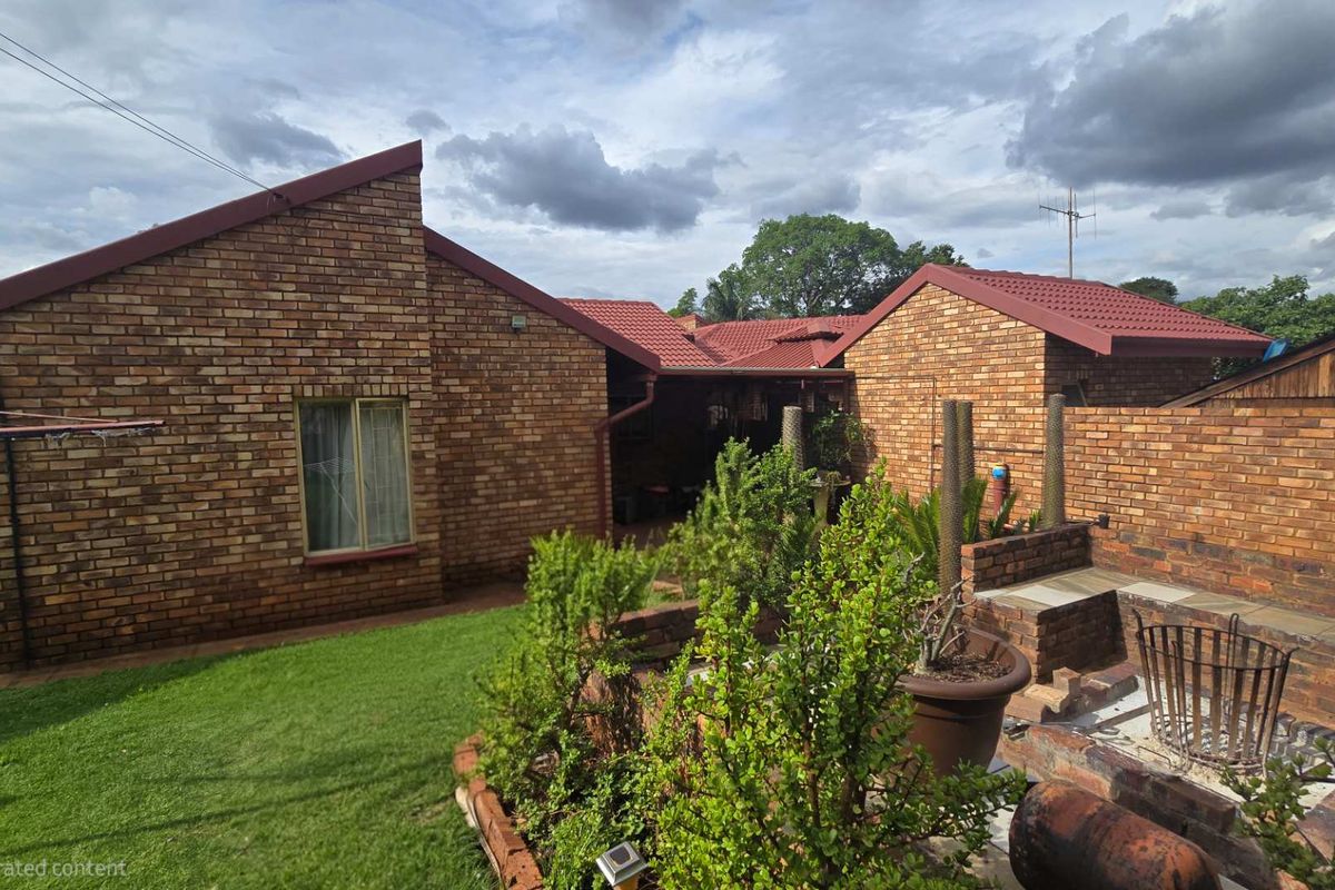 Rear view of the property featuring a face brick facade, tiled roof, and a built-in brick braai area set within a garden.
