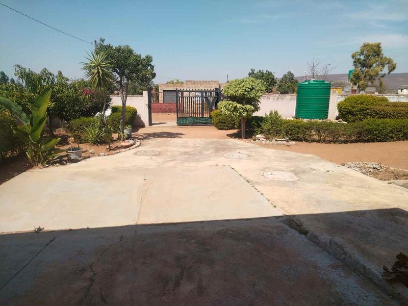 Front exterior view featuring a concrete driveway, perimeter wall with metal gate, and a water storage tank set within a landscaped garden area.