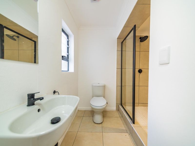 A clean, modern bathroom featuring a walk-in shower with black-framed glass, a wall-mounted basin with black fixtures, and neutral floor tiling.