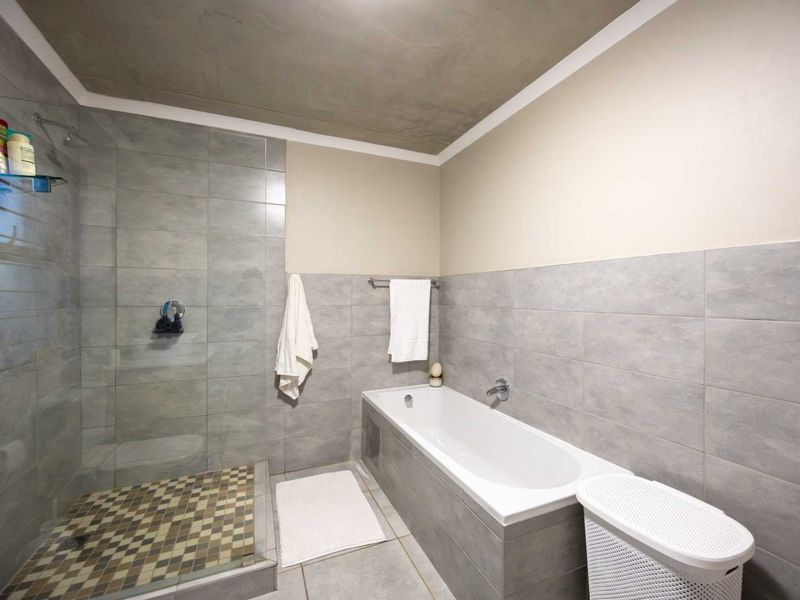 Modern bathroom featuring a walk-in shower with mosaic floor tiles, a built-in bathtub, and neutral grey wall tiling throughout.