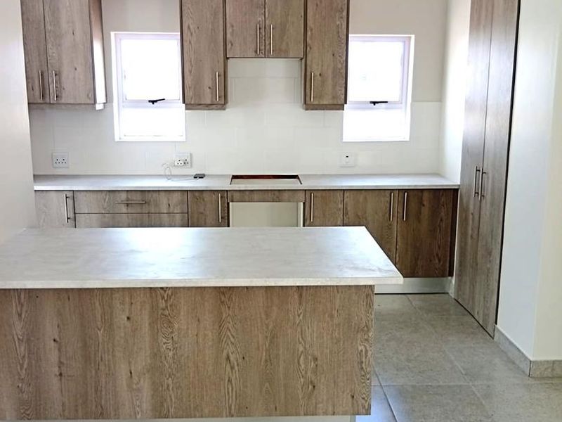Modern kitchen featuring wood-look cabinetry, stone-look countertops, a central island, and tiled flooring, offering a clean and functional workspace.