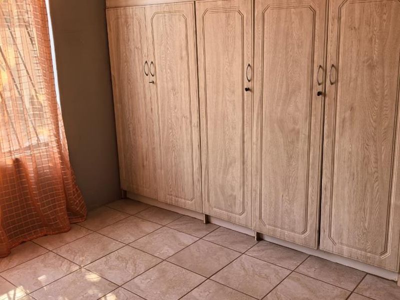 A bedroom featuring extensive built-in wooden cupboards and neutral tiled flooring, offering ample storage space.