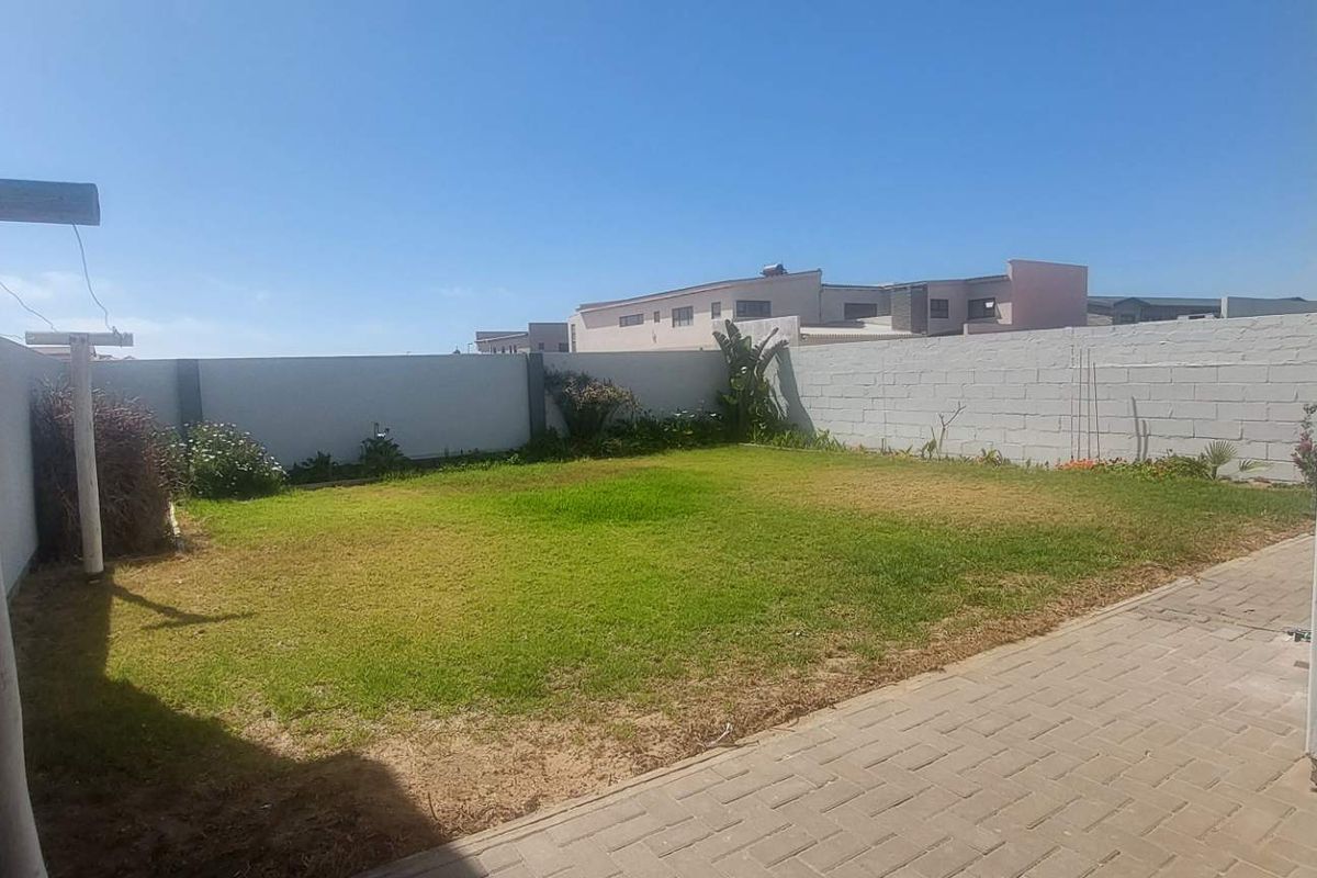 A private rear garden featuring a paved patio area and a lawn enclosed by boundary walls.