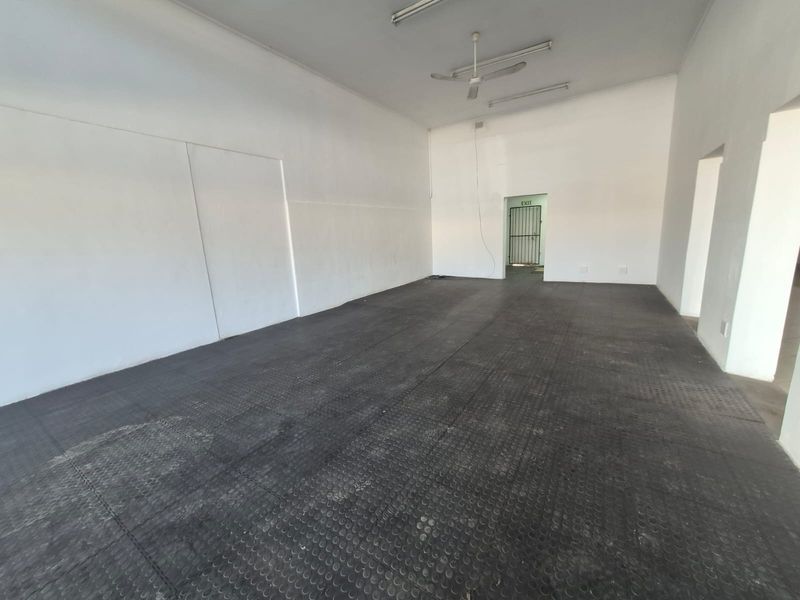 A spacious, empty open-plan commercial area featuring durable rubber flooring, ceiling fans, and fluorescent lighting, suitable for various business or retail uses.