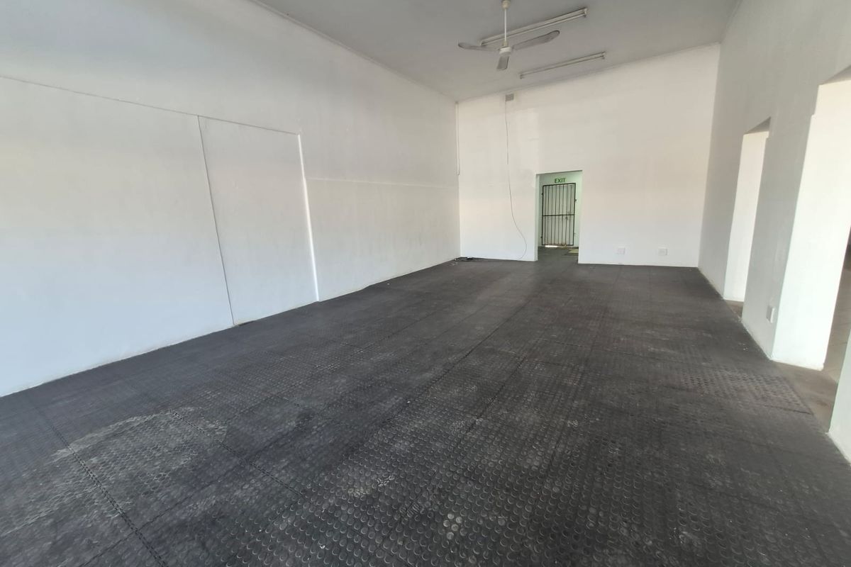 A spacious, empty open-plan commercial area featuring durable rubber flooring, ceiling fans, and fluorescent lighting, suitable for various business or retail uses.