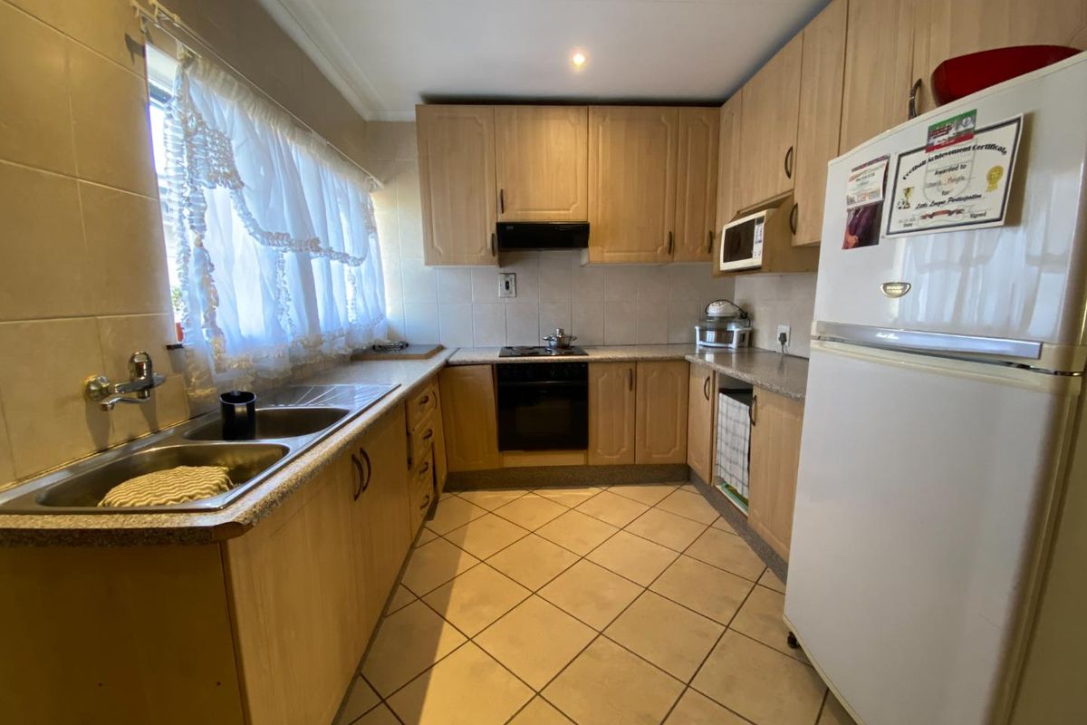 A functional kitchen featuring light wood cabinetry, tiled flooring, a double basin sink, and built-in oven with extractor fan.