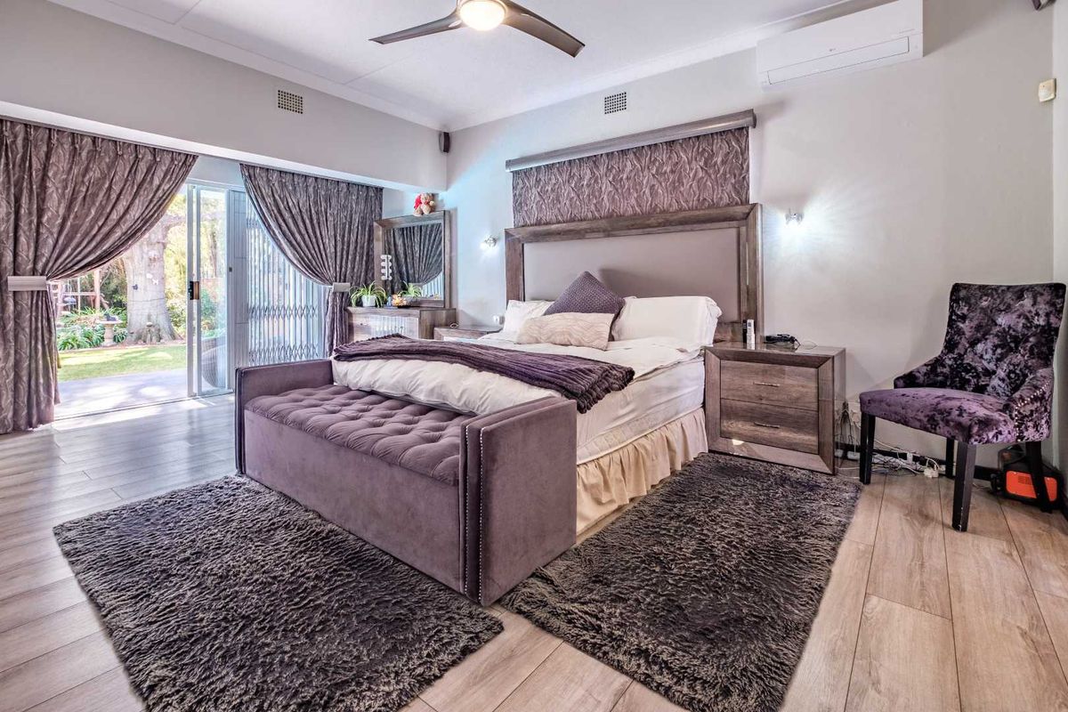 Spacious bedroom featuring wood-look flooring, a ceiling fan, wall-mounted air conditioning unit, and sliding glass doors providing direct access to the garden.