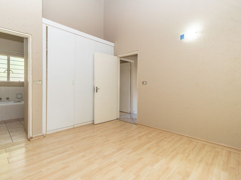 An empty bedroom featuring light laminate flooring, built-in cupboards, and direct access to an en-suite bathroom.