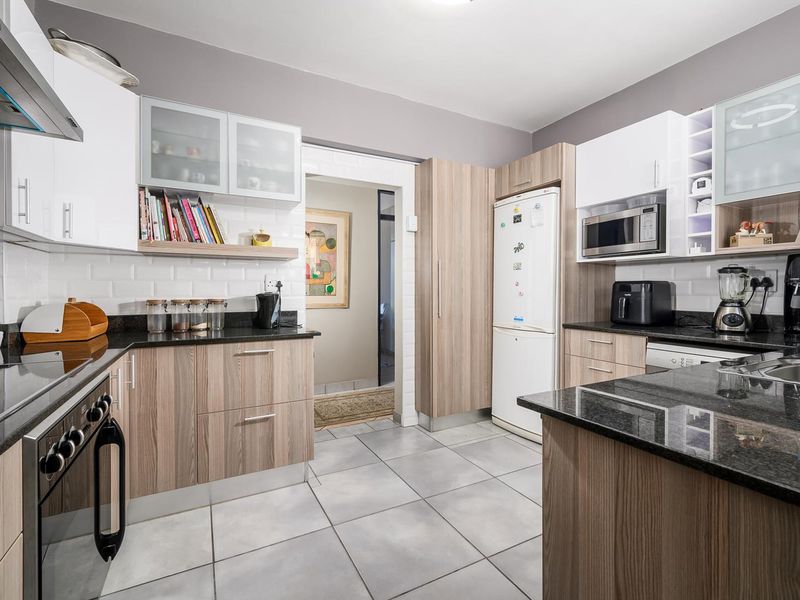 Modern kitchen featuring granite countertops, built-in oven, electric hob, extractor fan, and ample laminate cabinetry with a subway tile backsplash.