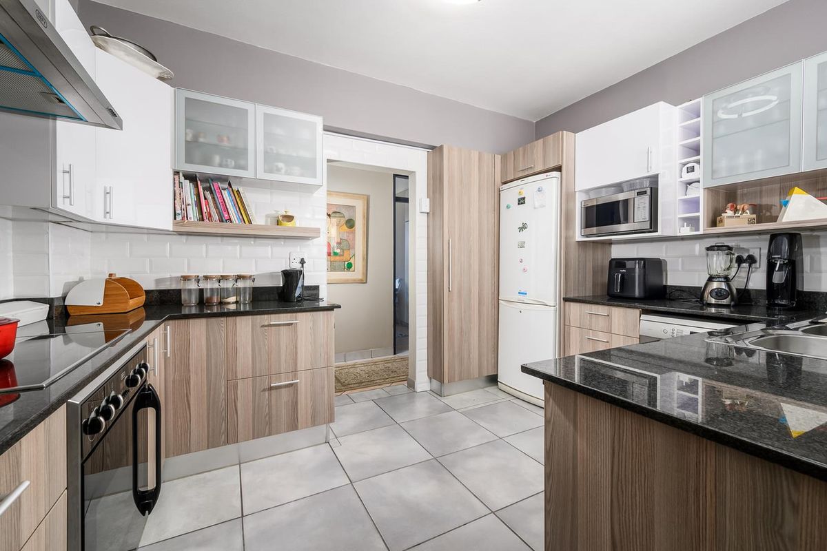 Modern kitchen featuring granite countertops, built-in oven, electric hob, extractor fan, and ample laminate cabinetry with a subway tile backsplash.