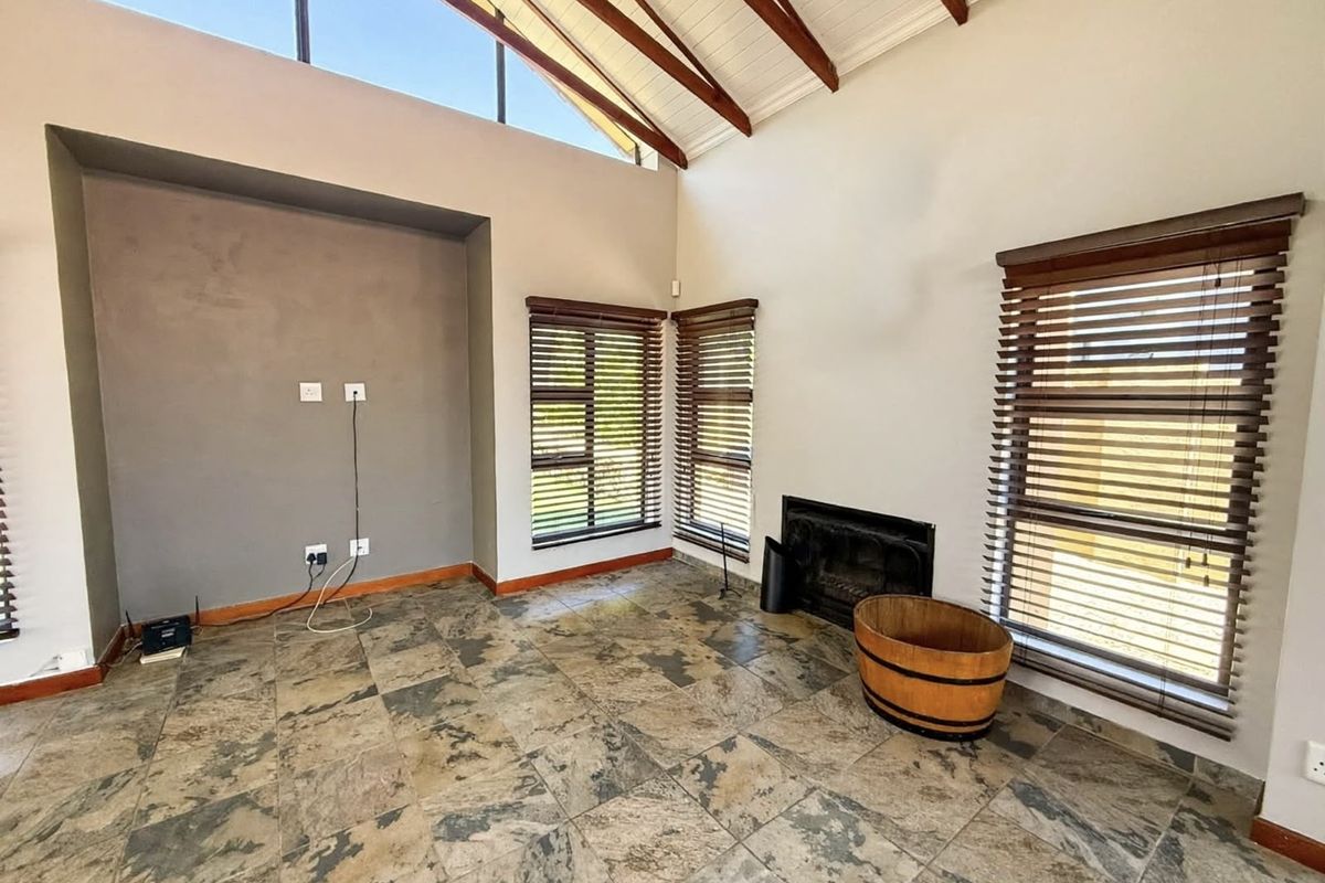 Spacious living room featuring vaulted ceilings with exposed timber beams, slate tile flooring, a built-in fireplace, and large windows with venetian blinds.