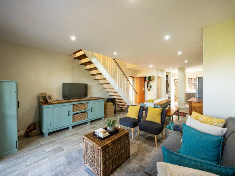 Open-plan living area featuring tiled flooring, recessed downlights, and a central staircase leading to the upper level.