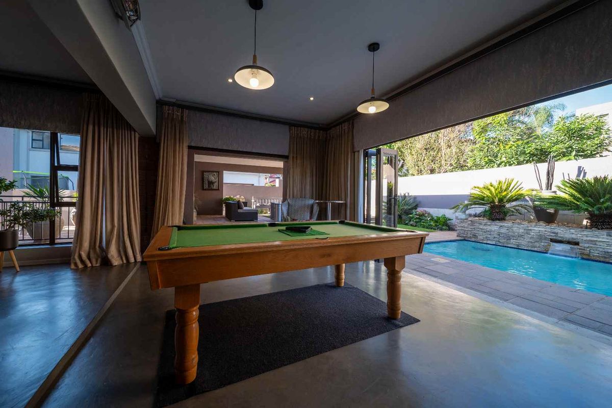 Spacious indoor entertainment area featuring polished concrete floors, pendant lighting, and large sliding doors opening directly onto a private swimming pool and garden.