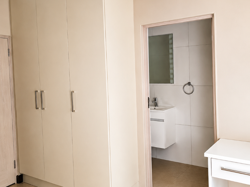 A clean, neutral bedroom featuring built-in cupboards and direct access to an en-suite bathroom with a modern vanity.