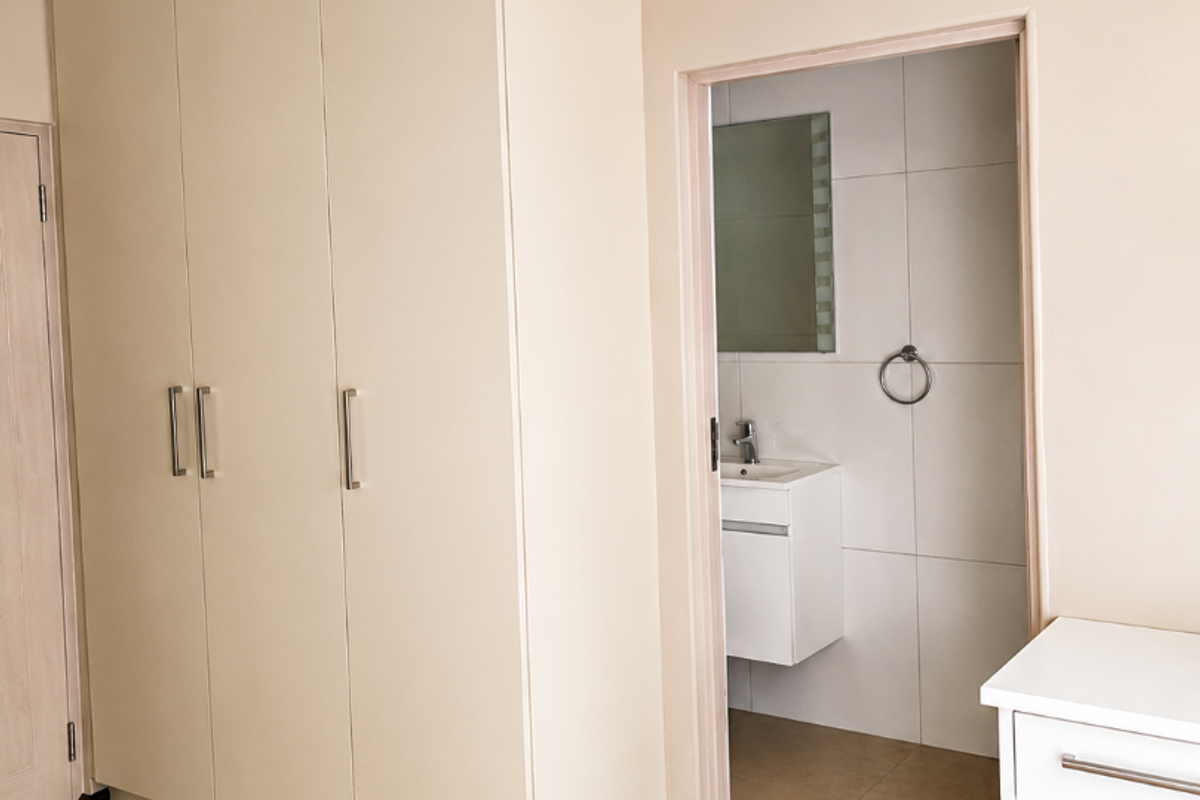 A clean, neutral bedroom featuring built-in cupboards and direct access to an en-suite bathroom with a modern vanity.