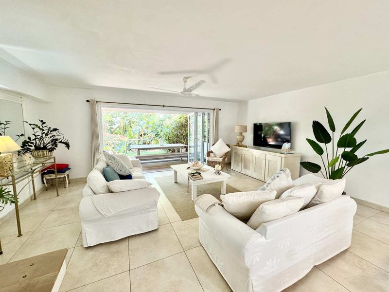 Spacious living room featuring neutral tiled flooring, a ceiling fan, and large stacking glass doors that open onto an outdoor patio area.
