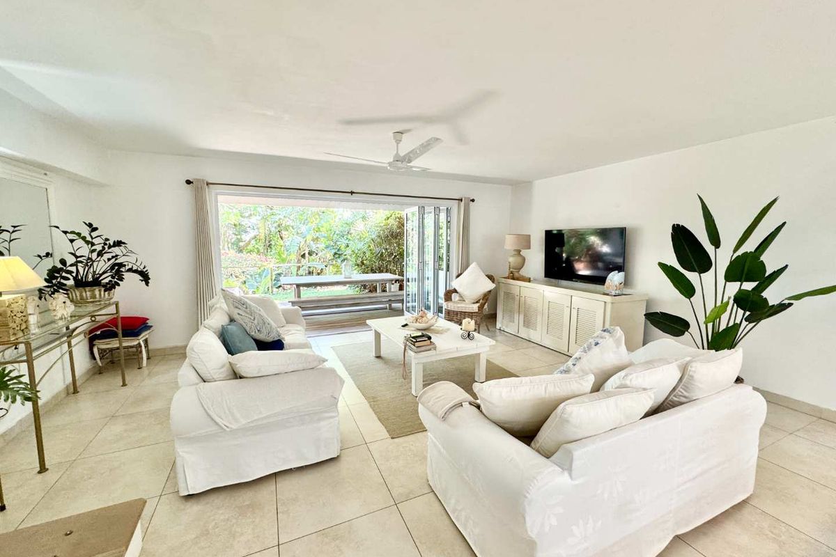Spacious living room featuring neutral tiled flooring, a ceiling fan, and large stacking glass doors that open onto an outdoor patio area.