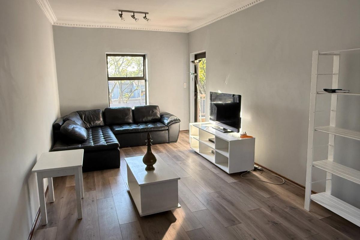 A living room featuring laminate flooring, decorative ceiling cornicing, and track lighting, providing a neutral base for interior design.