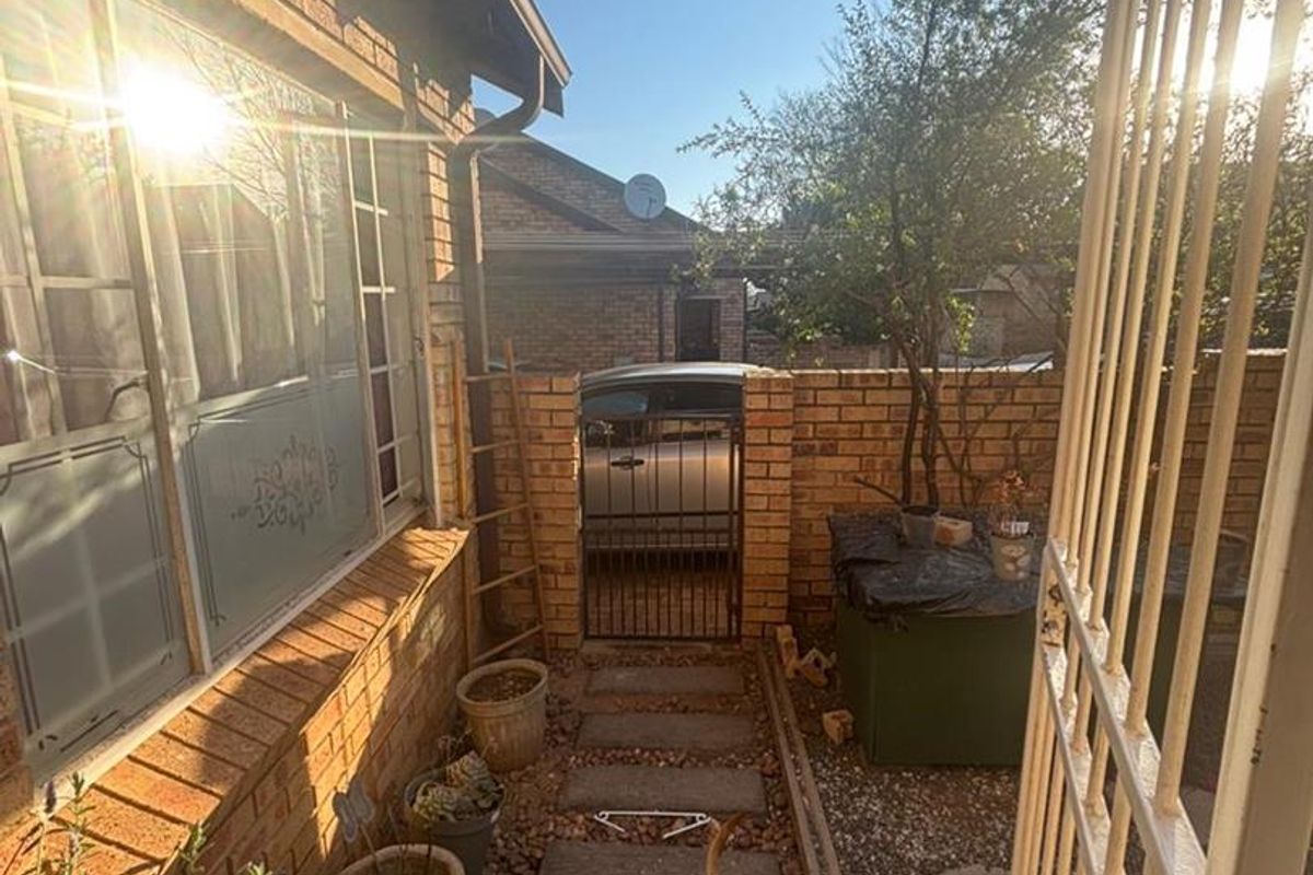 A side exterior walkway featuring brick walls, paved stepping stones, and a metal security gate leading to the driveway area.