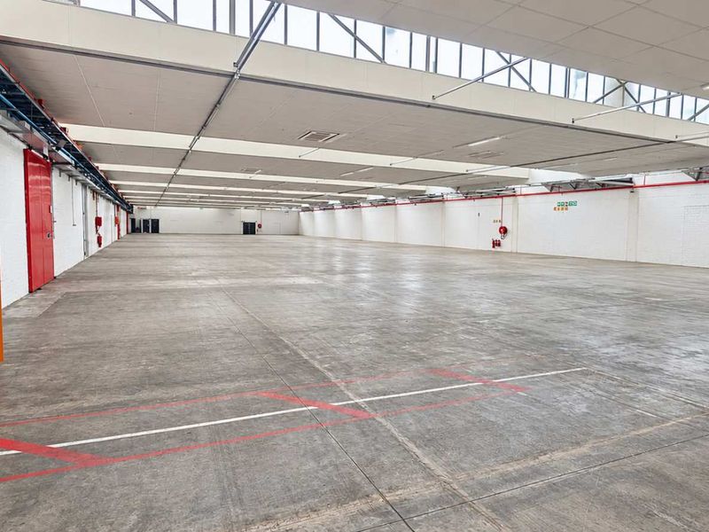 A spacious, open-plan industrial warehouse featuring concrete flooring, high ceilings with integrated skylights, and essential fire safety and electrical infrastructure.
