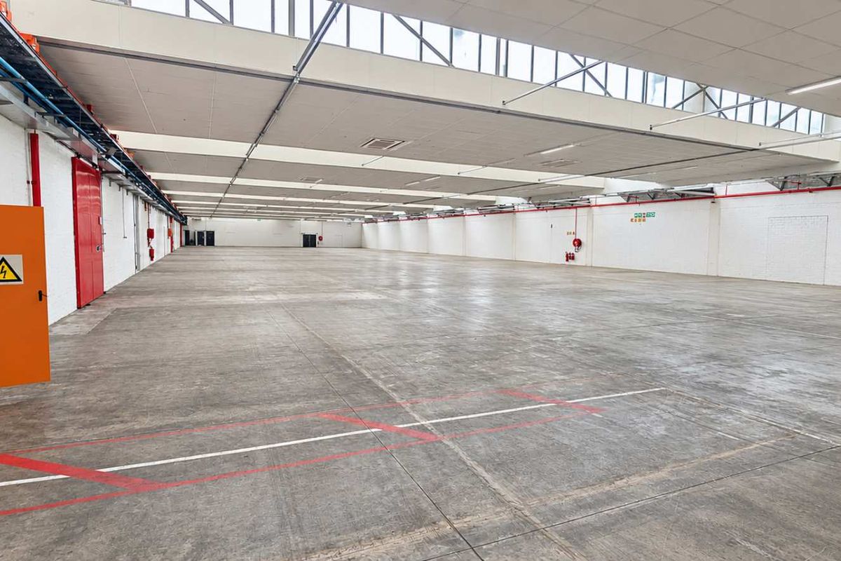 A spacious, open-plan industrial warehouse featuring concrete flooring, high ceilings with integrated skylights, and essential fire safety and electrical infrastructure.