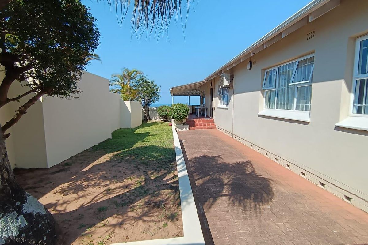 Rear exterior view featuring a paved walkway, a small lawn area, and a covered patio space with views toward the coast.