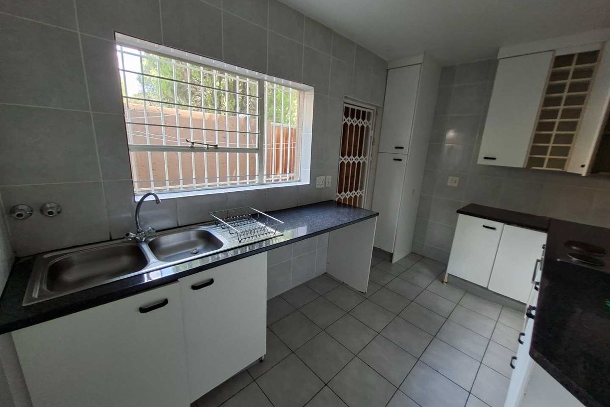A functional kitchen featuring tiled surfaces, double sink, and built-in cabinetry, offering a clean canvas for potential modern updates.