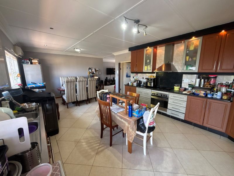 Open-plan kitchen and dining area featuring tiled flooring, wooden cabinetry, and integrated appliances, offering a functional layout for daily living and entertaining.