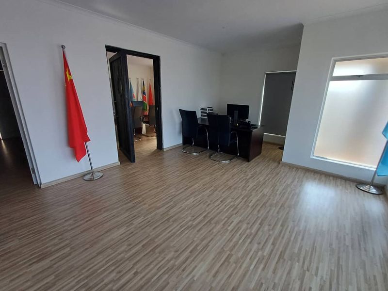 A professional office space featuring light wood-look laminate flooring, neutral walls, and large windows with roller blinds, providing a clean and functional work environment.