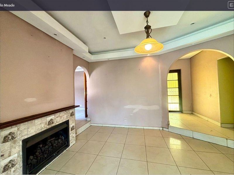 An empty living room featuring tiled flooring, a built-in fireplace with tiled surround, and architectural archways leading to adjacent spaces.