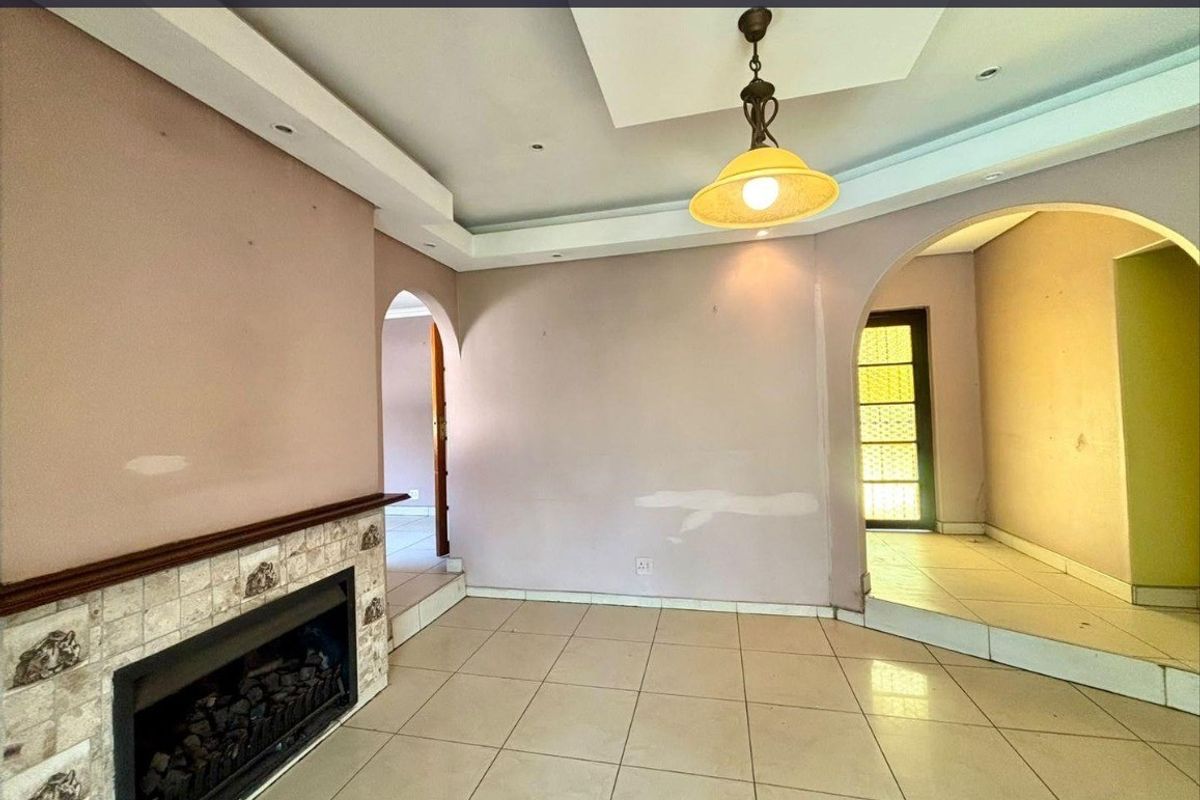 An empty living room featuring tiled flooring, a built-in fireplace with tiled surround, and architectural archways leading to adjacent spaces.
