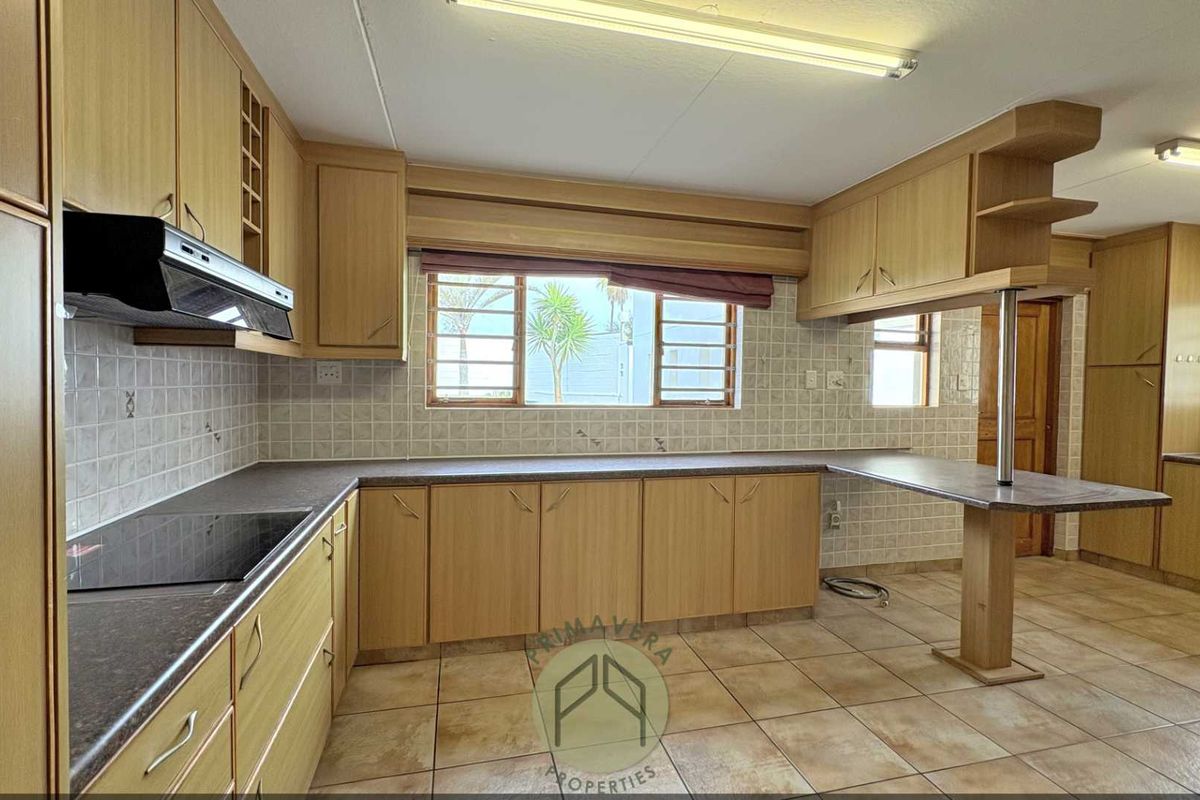A functional kitchen featuring laminate cabinetry, a breakfast bar, built-in hob, and extractor fan, finished with ceramic tile flooring and backsplash.