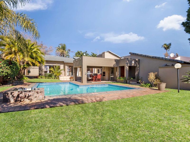 Rear exterior view featuring a swimming pool, a covered patio area, and a well-maintained garden with brick paving.