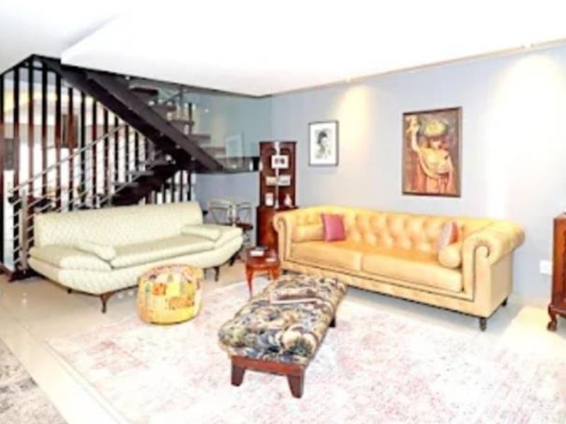 Spacious living room featuring a modern staircase with glass balustrade, recessed lighting, and neutral tiled flooring.