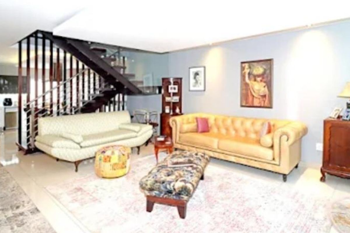 Spacious living room featuring a modern staircase with glass balustrade, recessed lighting, and neutral tiled flooring.