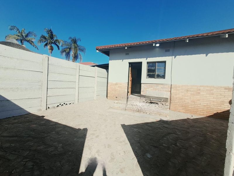 Rear exterior view of the property featuring a brick and plaster facade, tiled roof, and a precast concrete boundary wall with an unpaved yard.