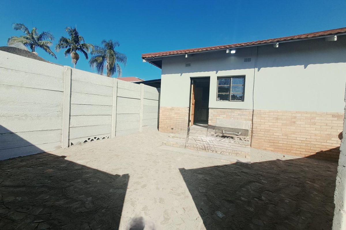 Rear exterior view of the property featuring a brick and plaster facade, tiled roof, and a precast concrete boundary wall with an unpaved yard.