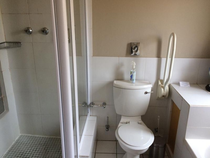 A functional bathroom featuring a shower enclosure, toilet, and wall-mounted grab rail with neutral tiled finishes.