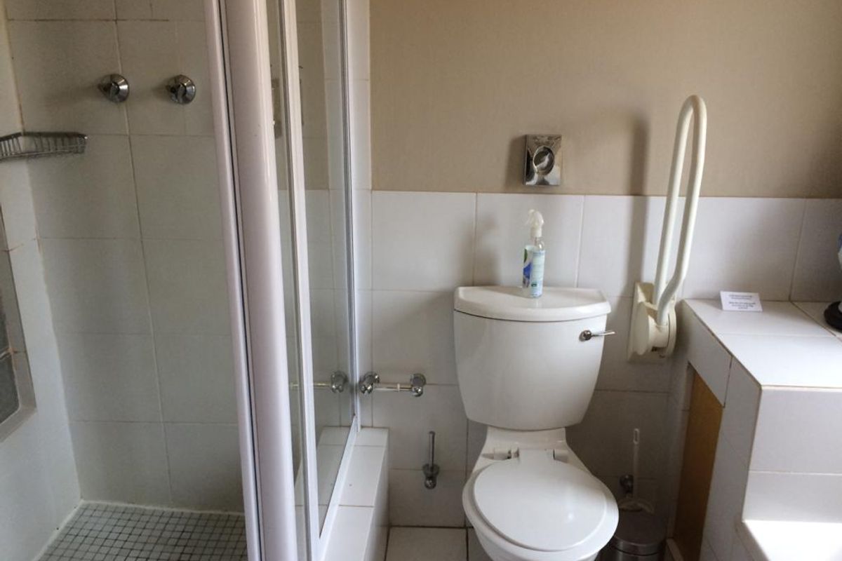 A functional bathroom featuring a shower enclosure, toilet, and wall-mounted grab rail with neutral tiled finishes.