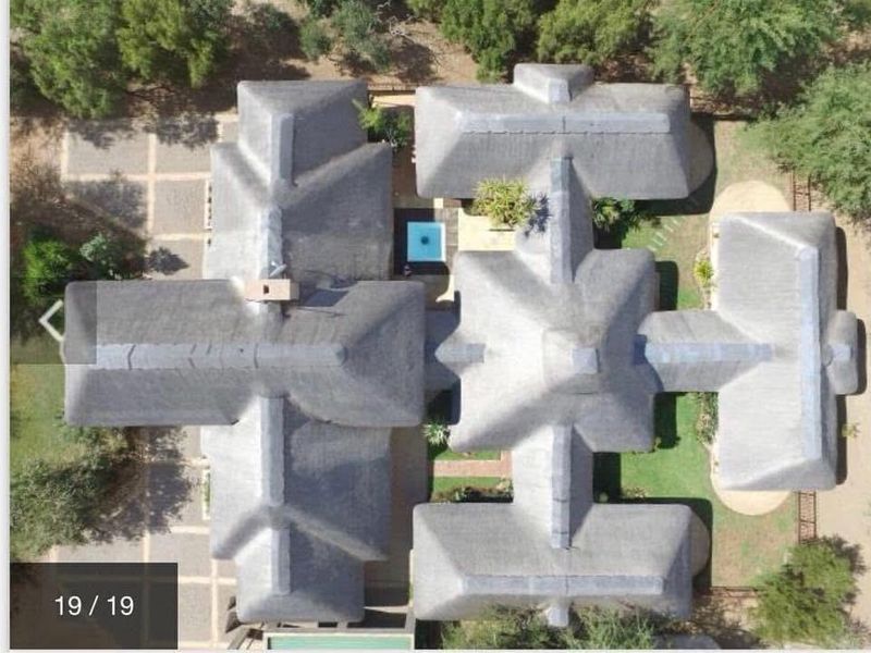 Aerial view of the property showcasing the extensive thatched roof layout, central swimming pool, and surrounding landscaped grounds.