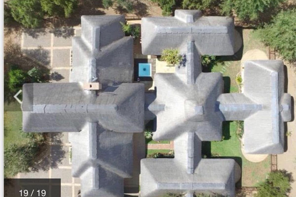 Aerial view of the property showcasing the extensive thatched roof layout, central swimming pool, and surrounding landscaped grounds.