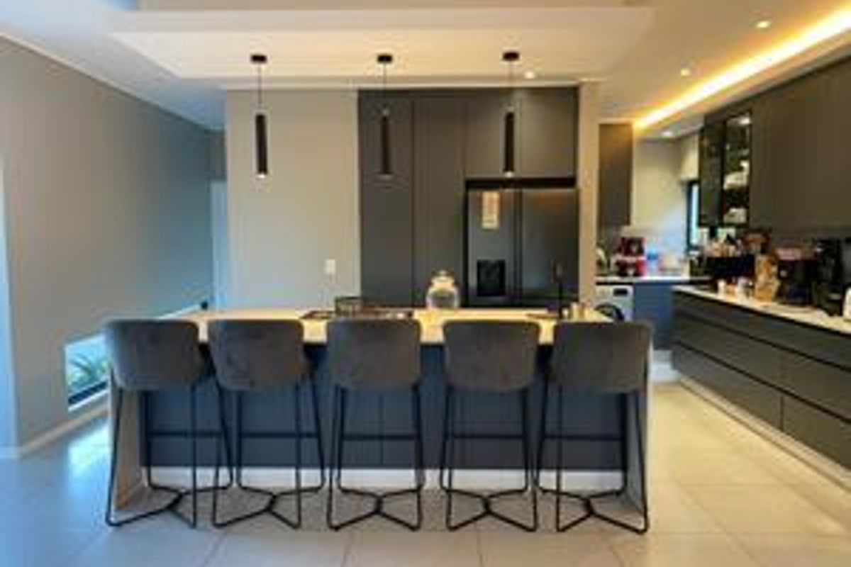 Modern kitchen featuring a large central island with stone countertops, sleek dark cabinetry, recessed lighting, and high-end integrated fixtures.