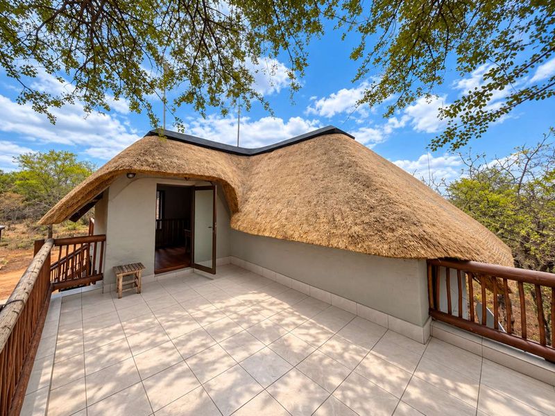A spacious elevated balcony featuring a traditional thatched roof, tiled flooring, and wooden balustrades, offering an open-air outdoor living space.